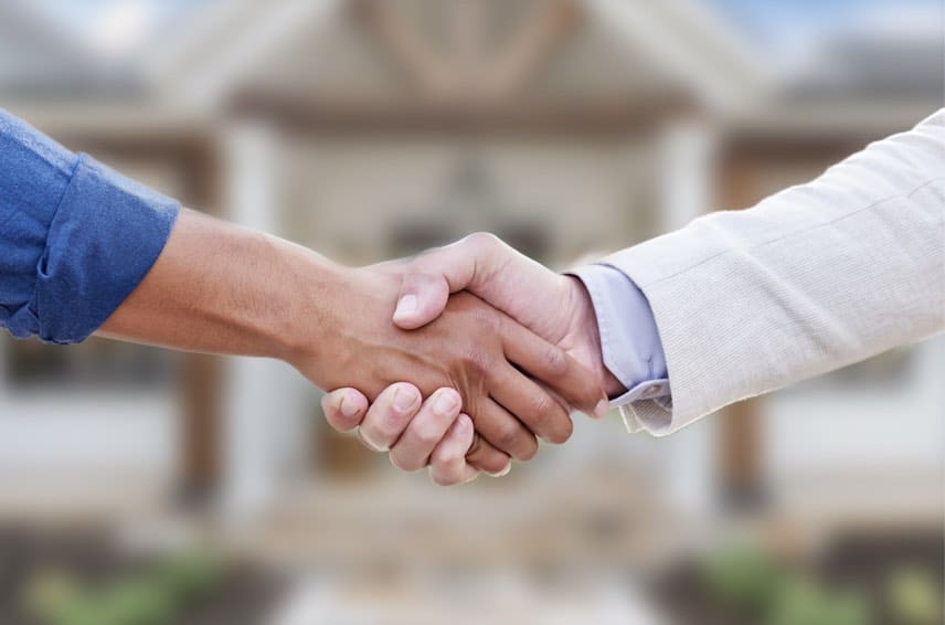 Handshake closing a home sale in front of a house