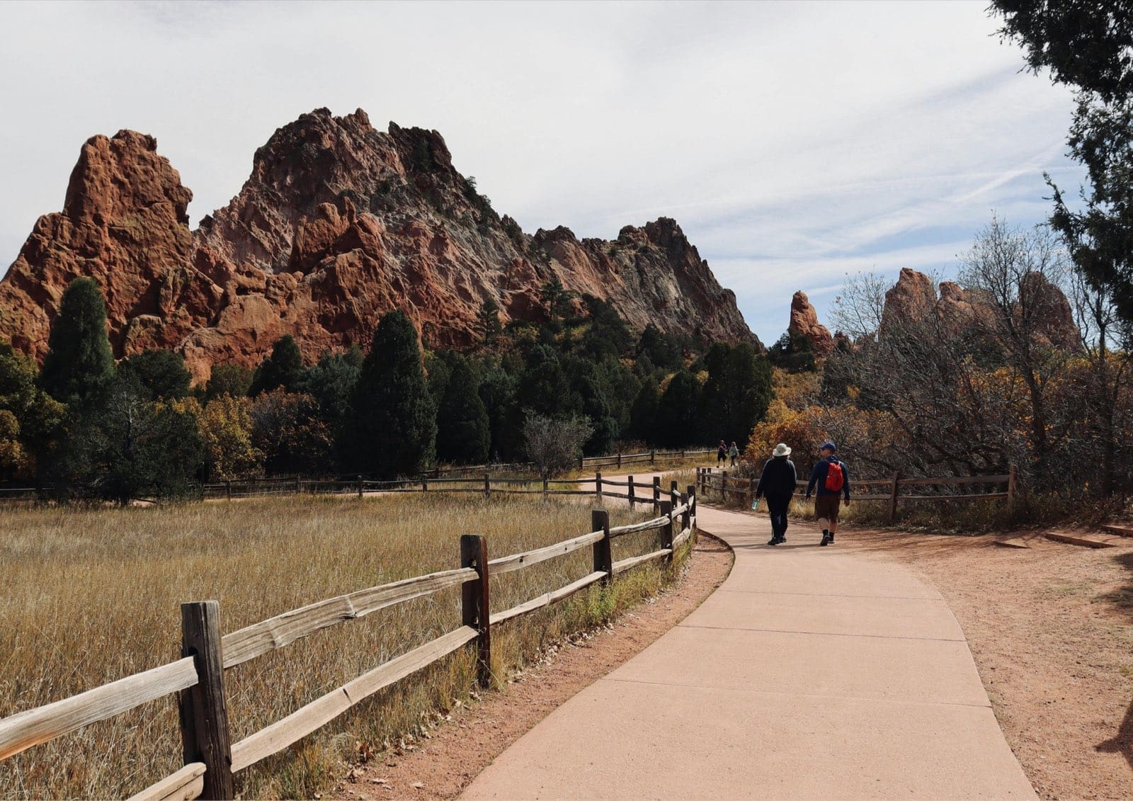 Red sandstone formations rise above a fenced walking path with hikers at Garden of the Gods.