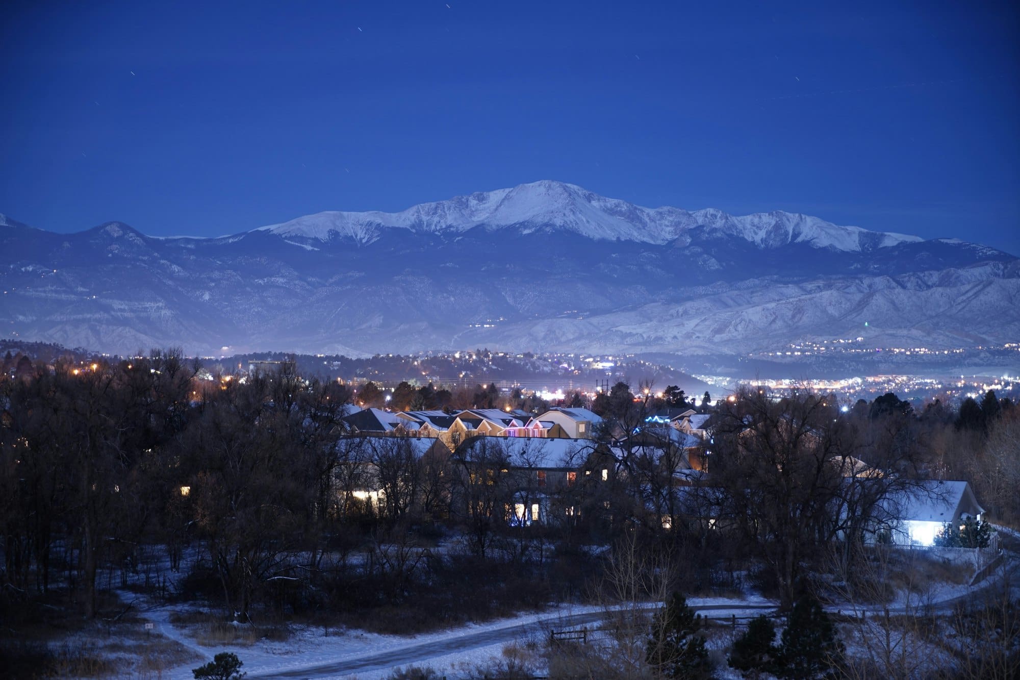 Colorado Springs neighborhood at dusk with snow-covered Pikes Peak behind it